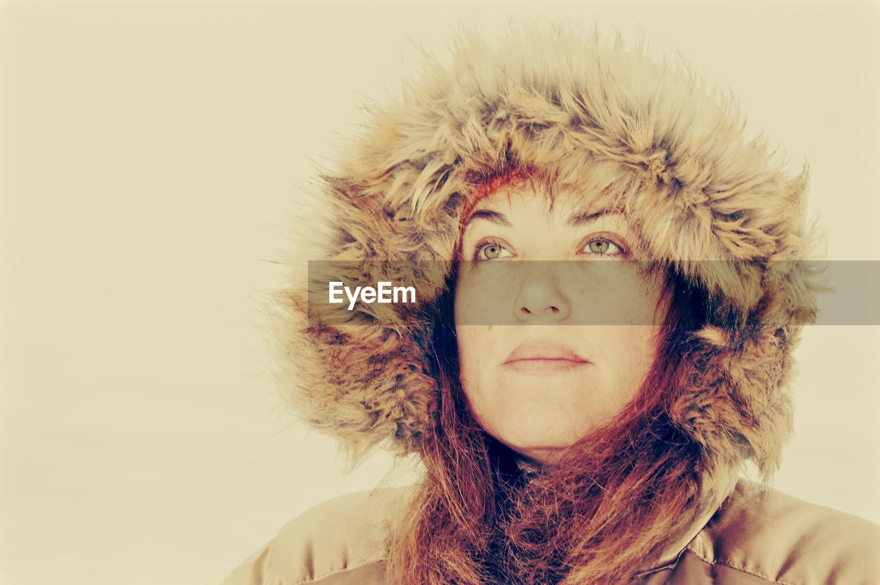 Close-up of thoughtful mature woman in warm clothing looking away against beige background