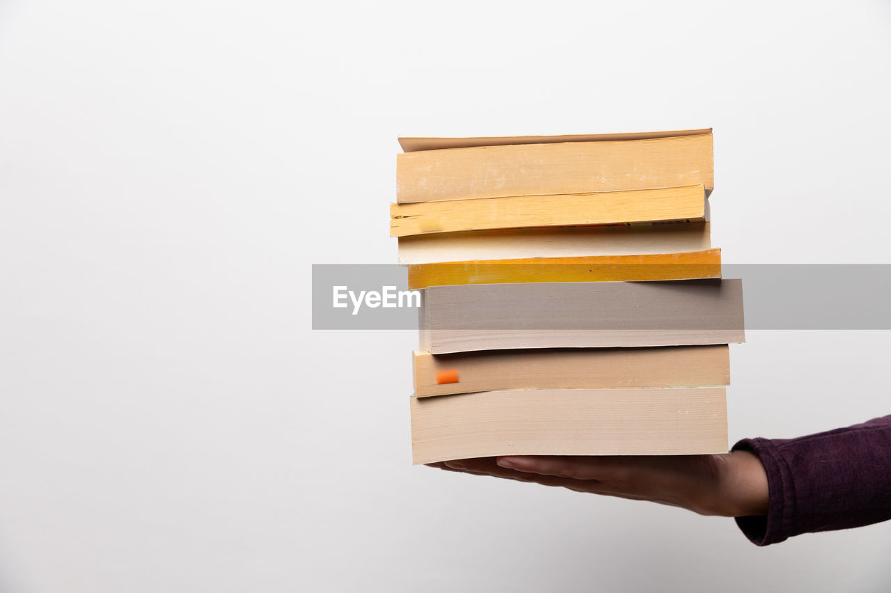 Hands holding books on white background, close-up. stack of different books lies on girl's hand