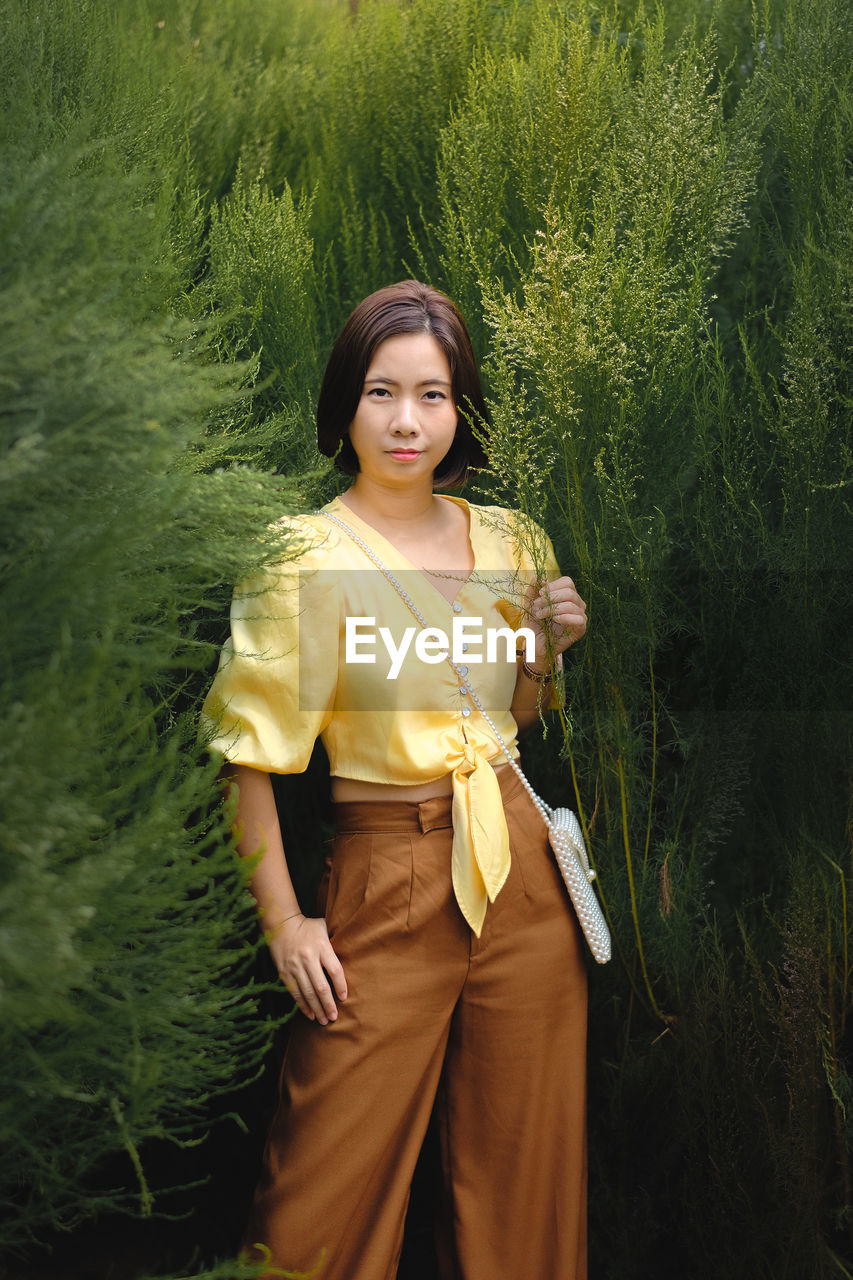 Portrait of young woman standing against trees