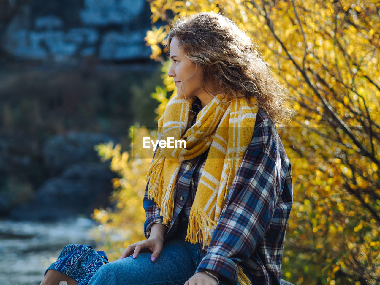 Pretty curly woman in plaid shirt sitting with a yellow tree on a background 