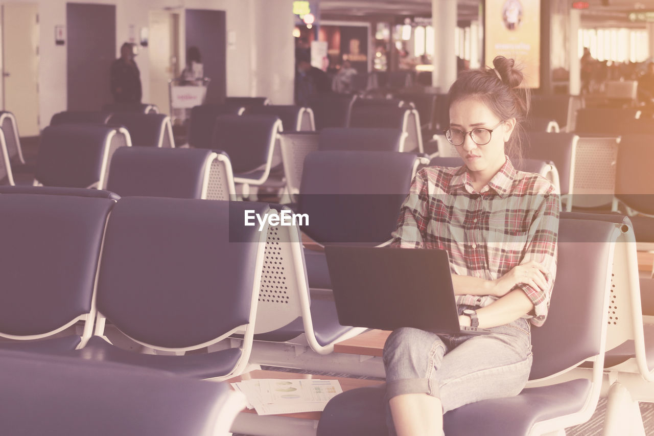 Woman using laptop while sitting at airport departure area