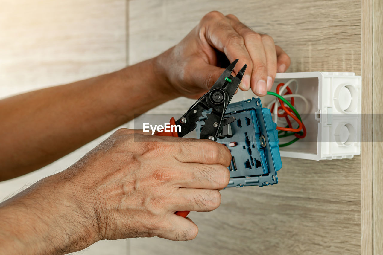 Stripping electrical wires in a plastic box on a wooden wall to install the electrical outlet.