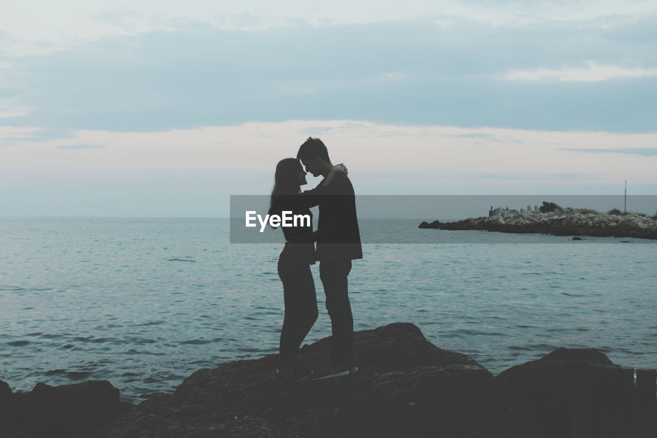 Couple kissing on sea against sky