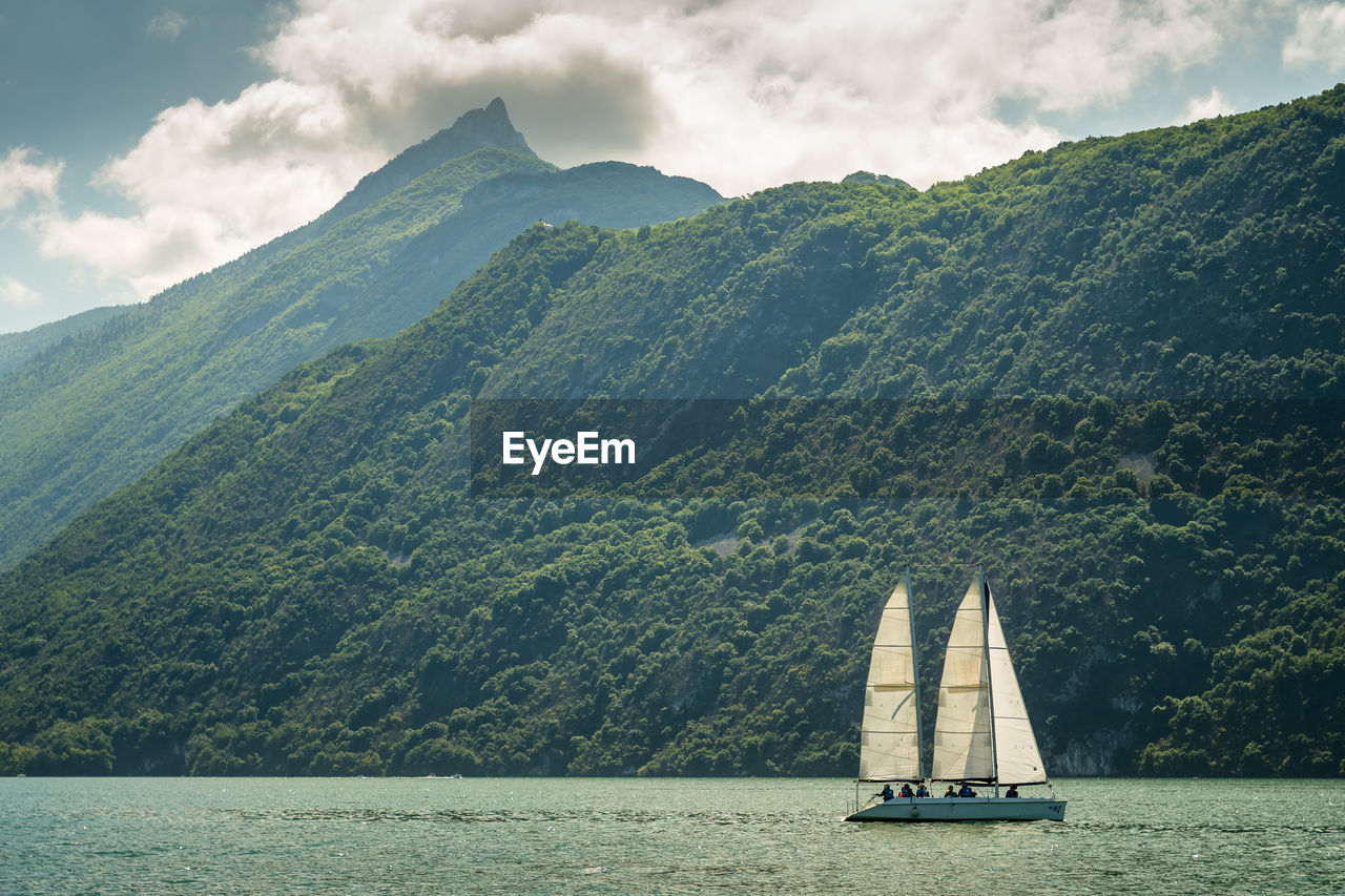 Sailboat sailing on sea by mountains against sky