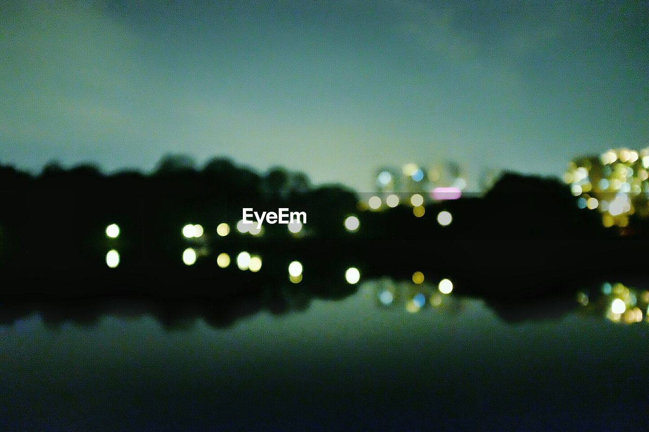 Defocused image of illuminated lights reflecting on lake at night