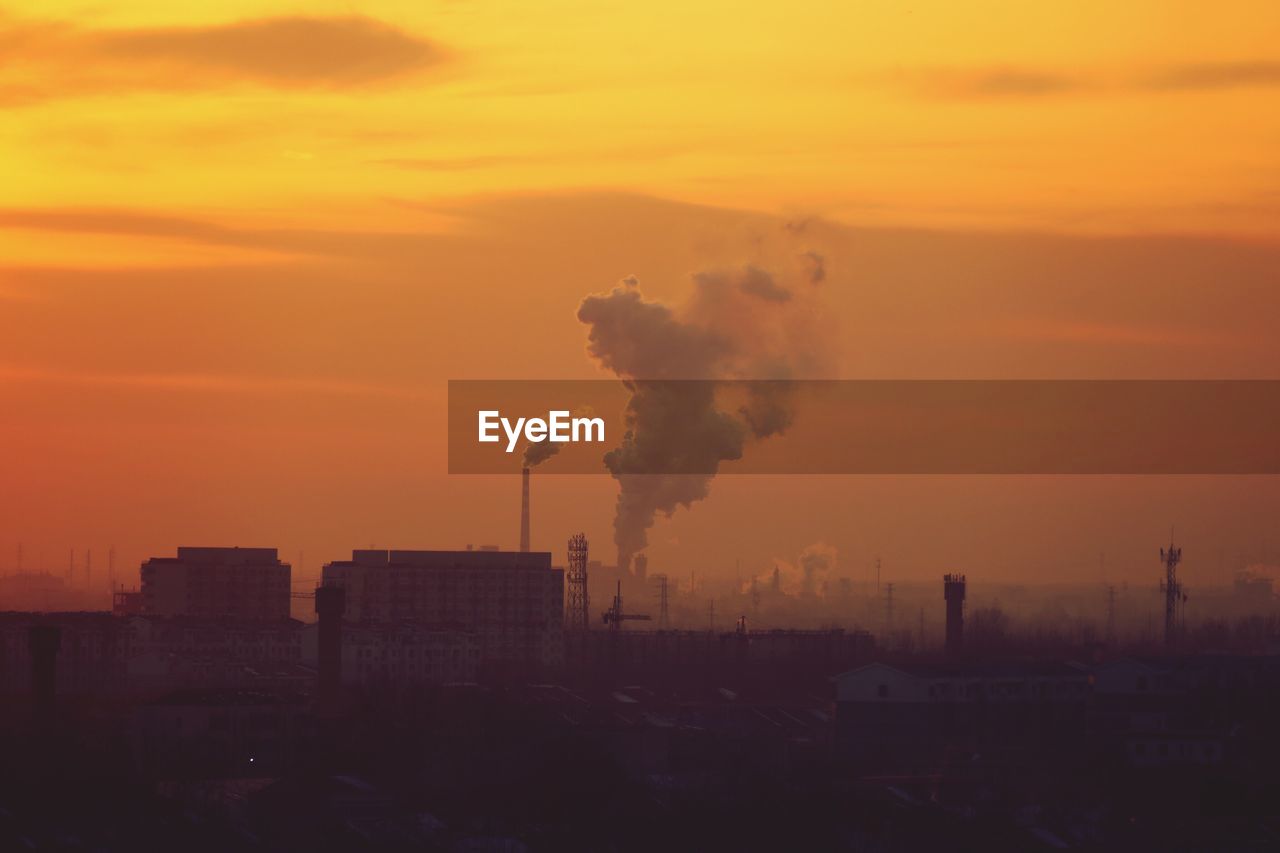 Smoke emitting from factories against sky during sunset