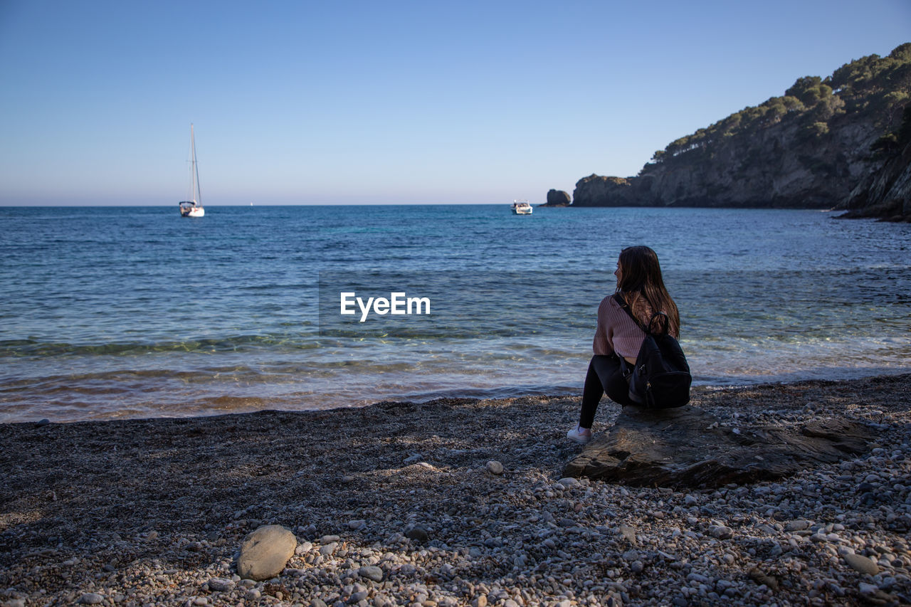 Beautiful women sitting on a rock at a pebble beach with copy space