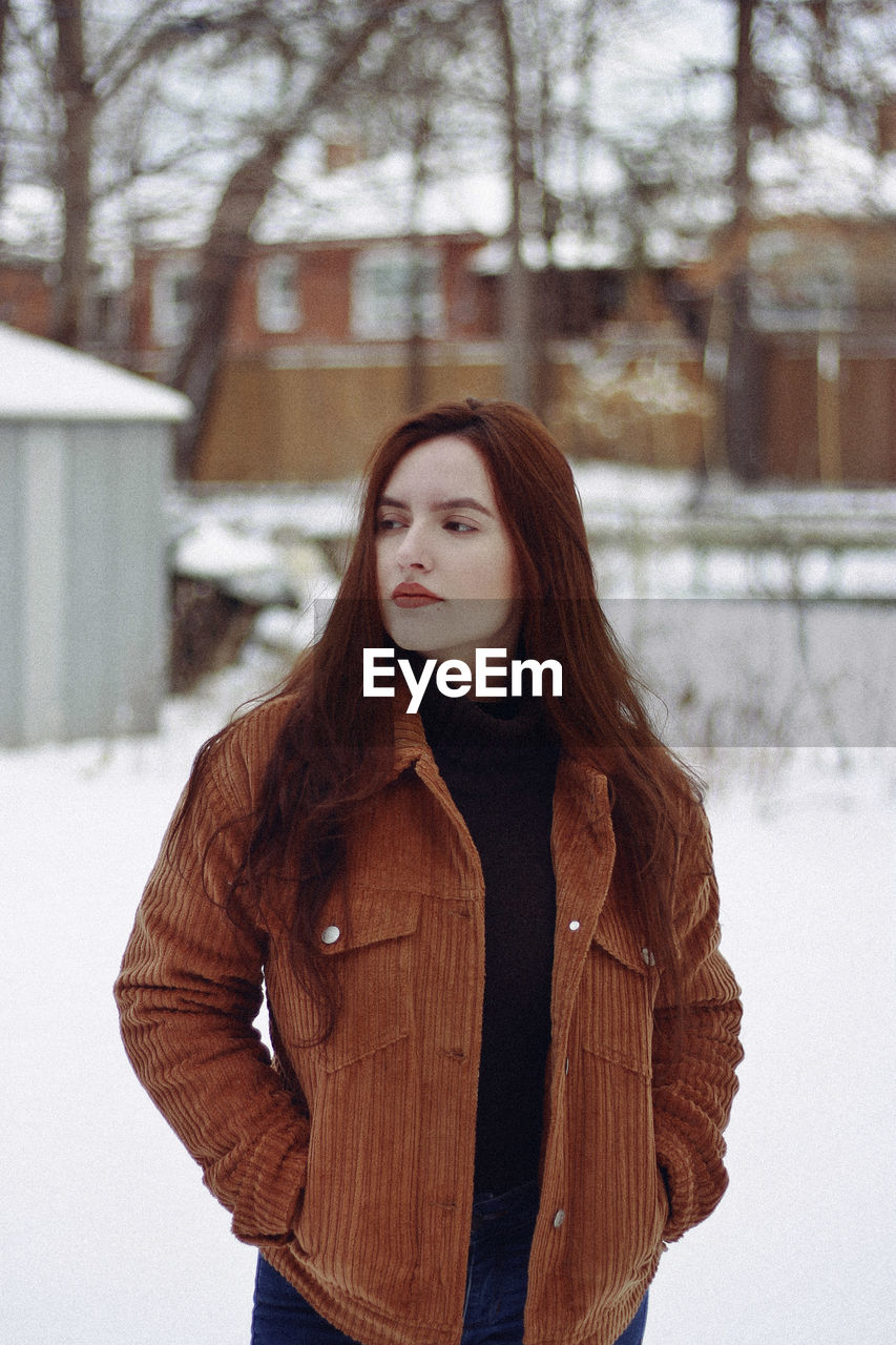 Young woman looking away while standing on snow covered field