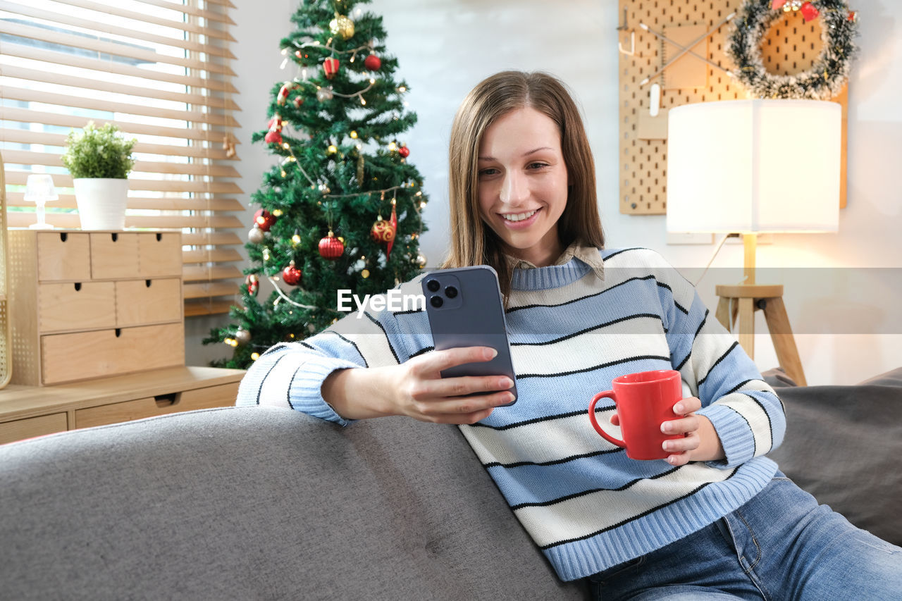 portrait of smiling woman using digital tablet while sitting on sofa at home