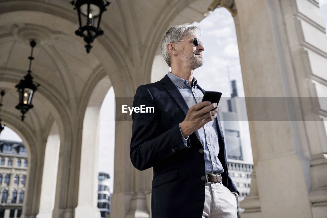 Grey-haired businessman in the city holding smartphone