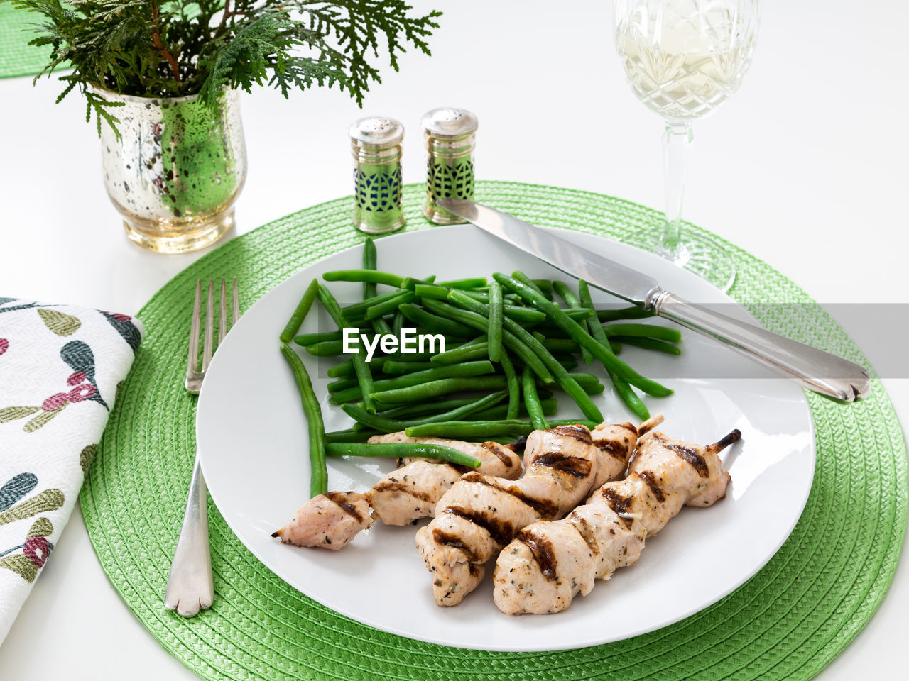 Healthy meal of chicken brochettes and green beans on white plate set on green placemat