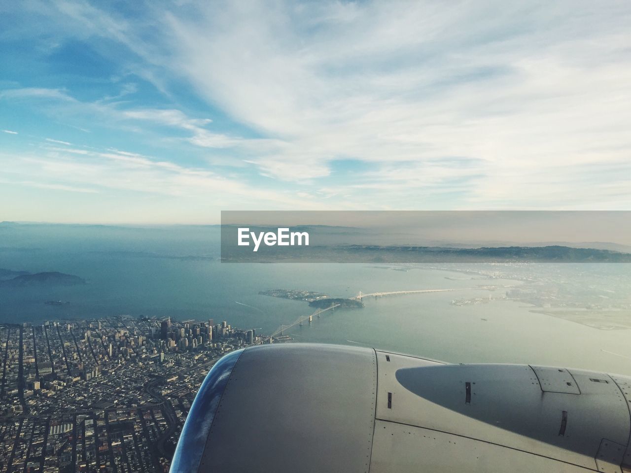 Cropped image of airplane flying over city and sea against sky