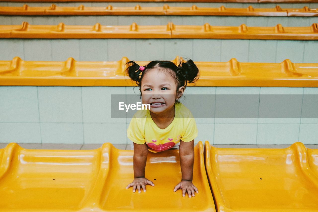 High angle view of cheerful girl leaning on yellow retaining wall