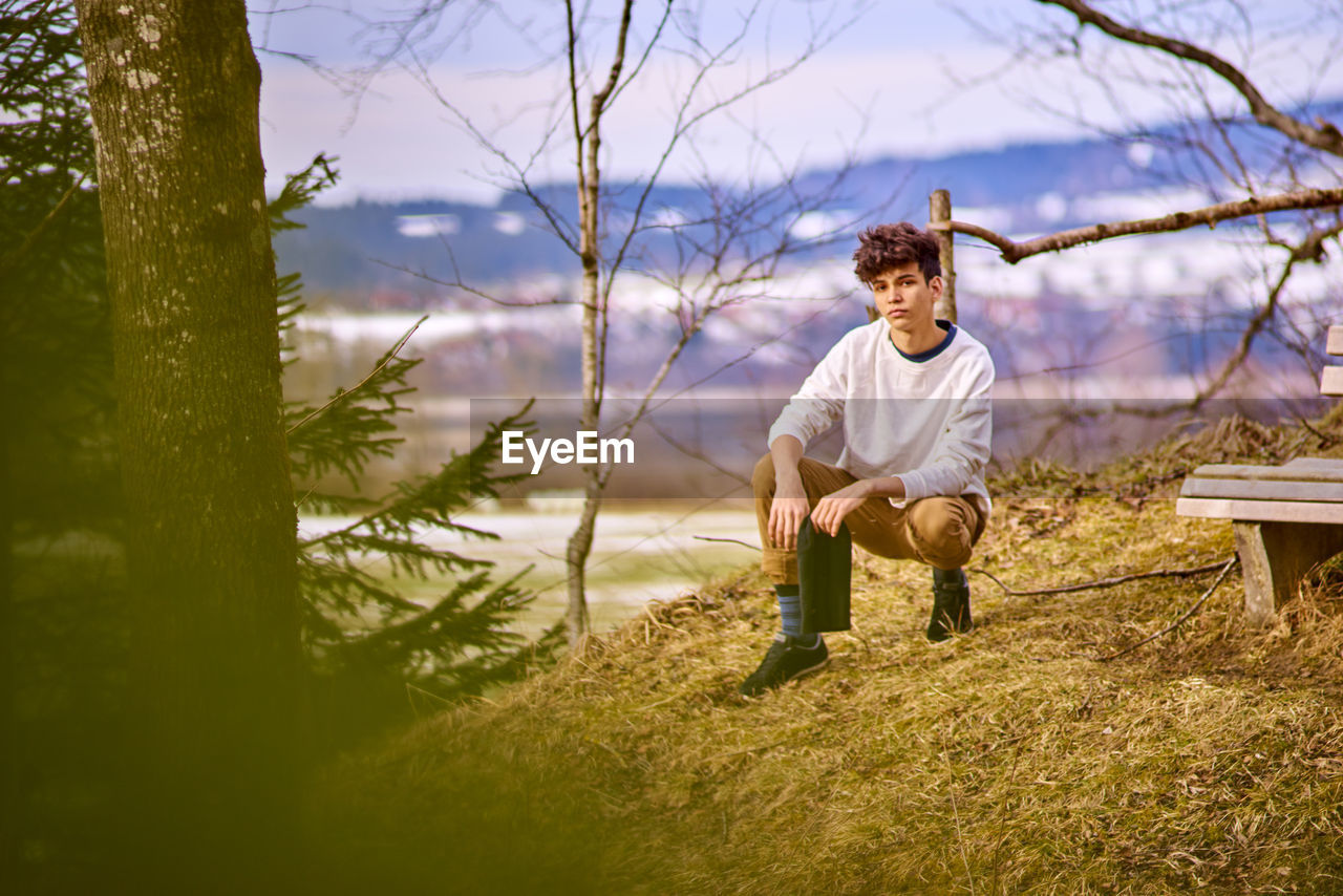 Young man crouching on field at forest