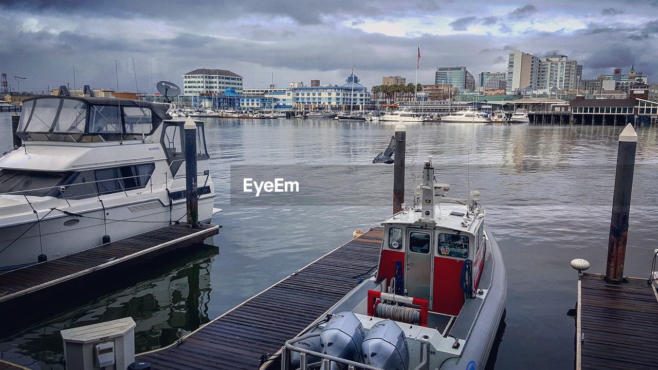 BOATS MOORED IN HARBOR BY CITY AGAINST SKY