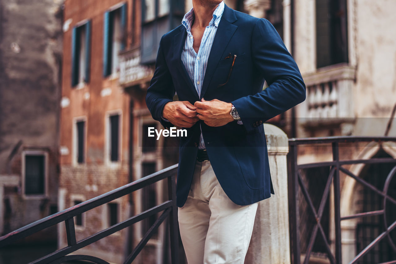 Midsection of man wearing blazer while standing against building