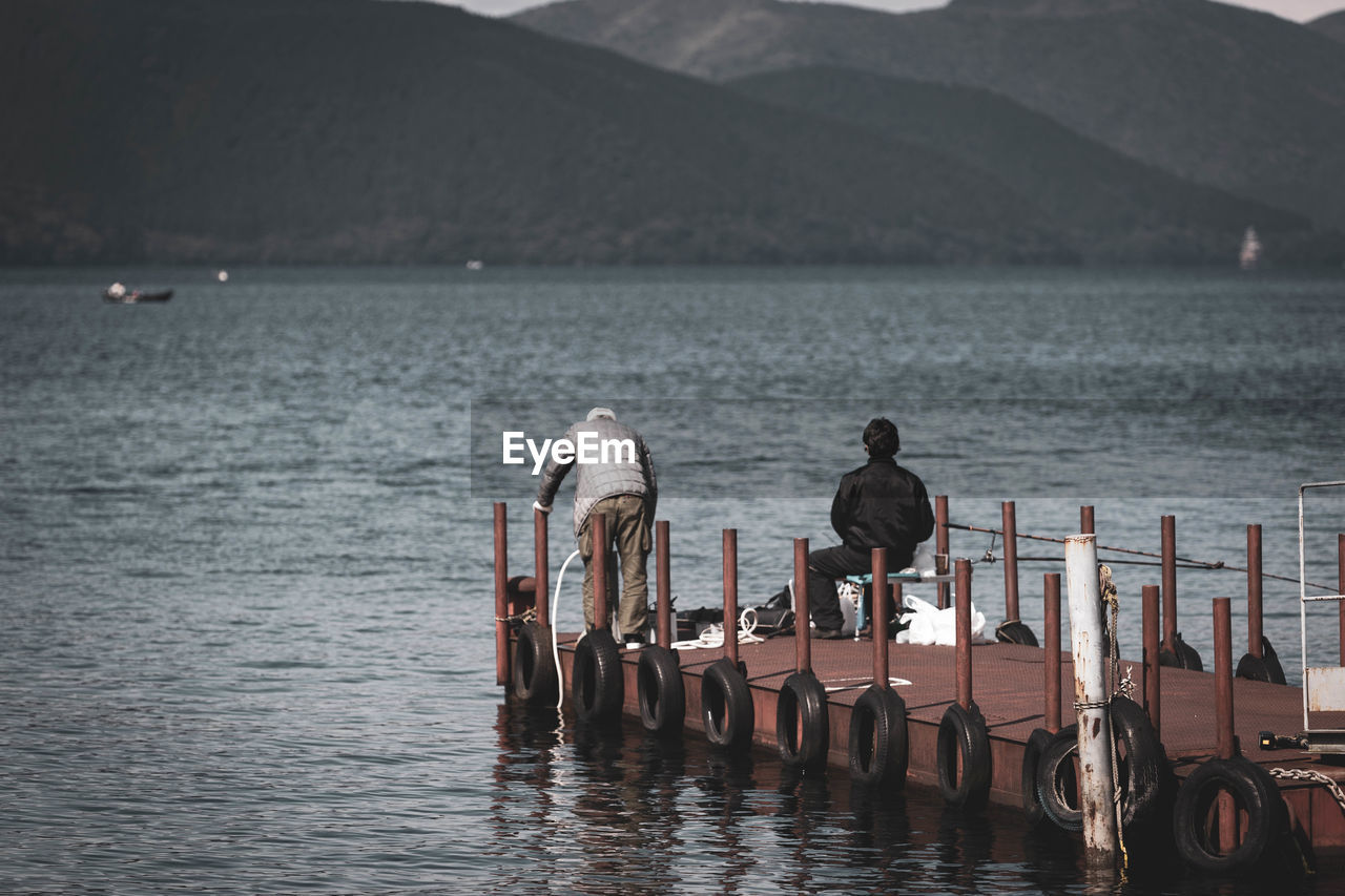 Rear view of men on pier by lake and mountains