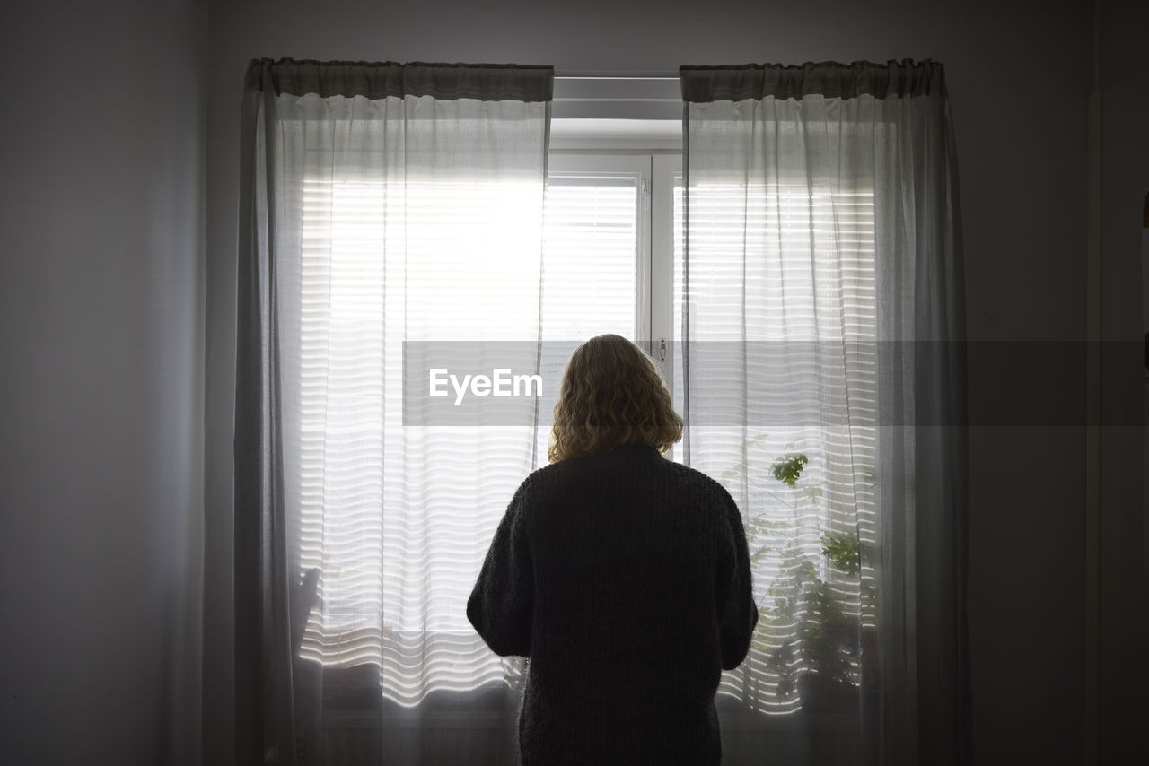 Rear view of teenage girl looking through window