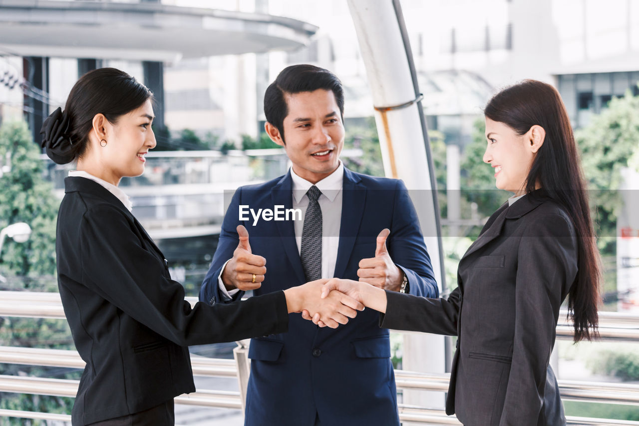 Businessman looking at colleagues giving handshake while standing in office