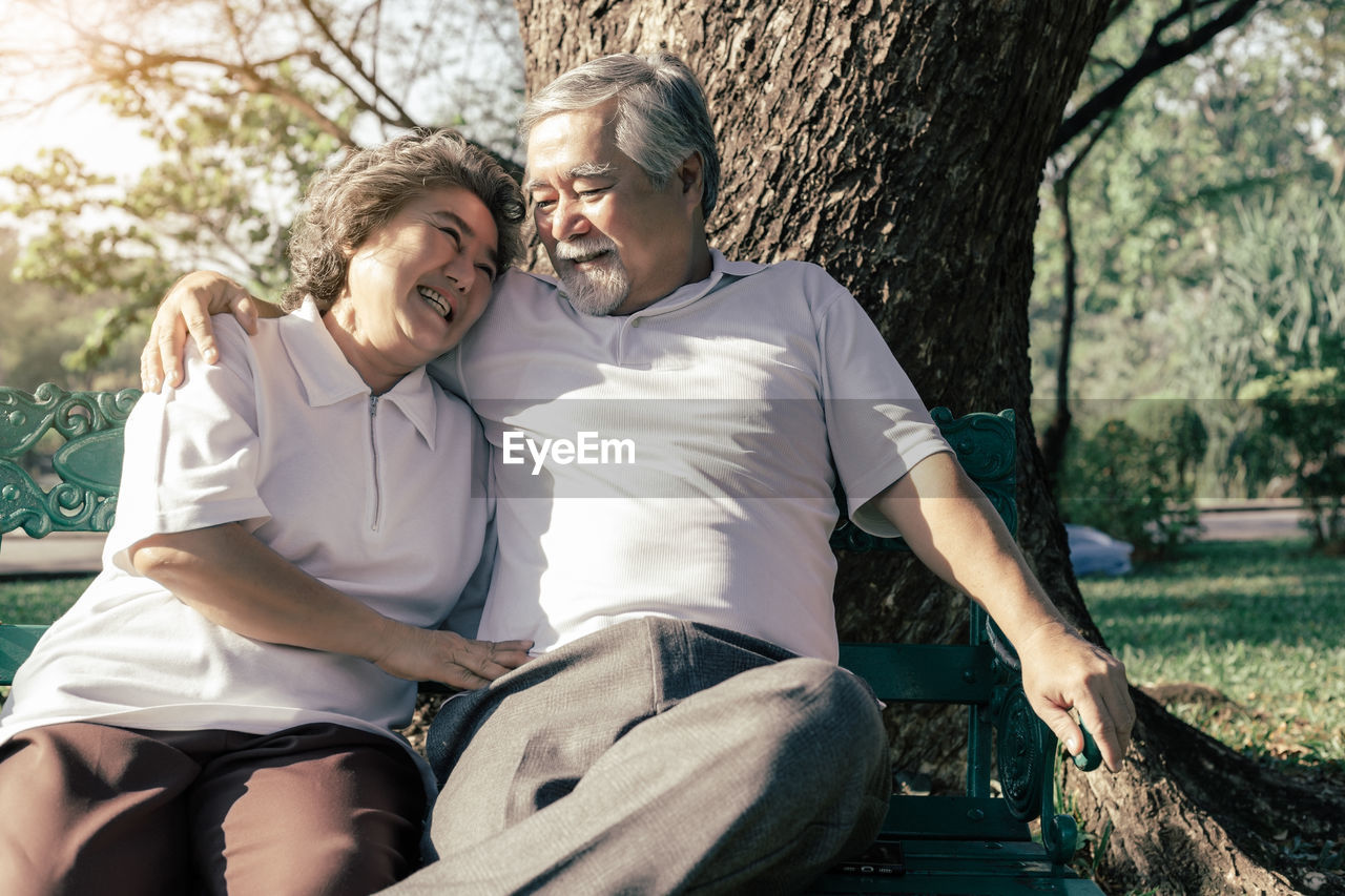 Smiling senior couple sitting by tree trunk