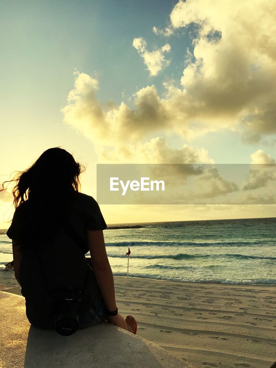 REAR VIEW OF WOMAN SITTING ON BEACH