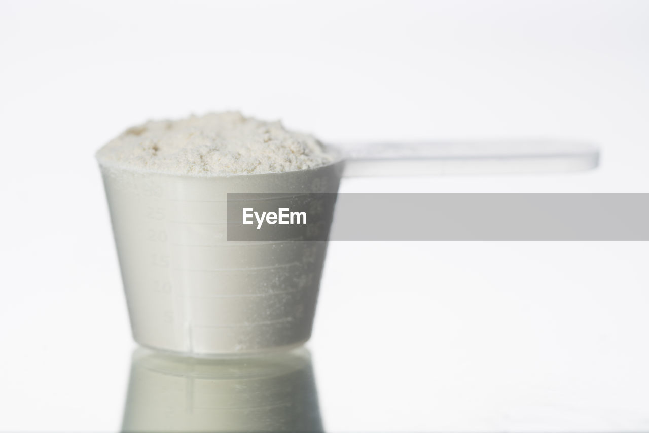 Close-up of nutritional supplement in measuring cup against white background