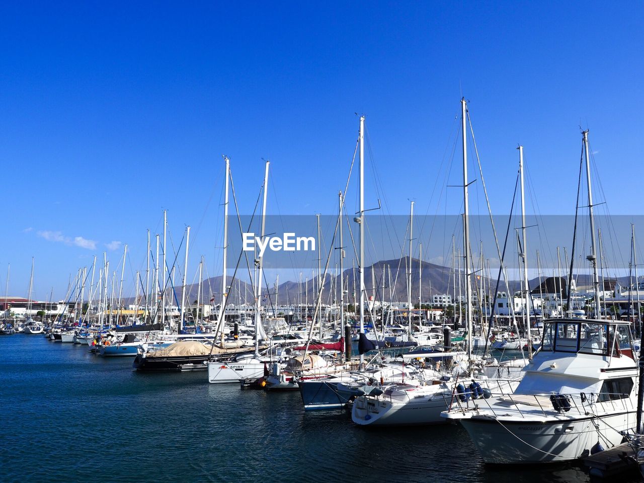 SAILBOATS MOORED IN SEA AGAINST CLEAR BLUE SKY