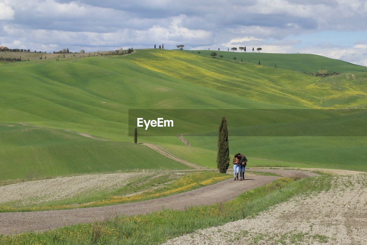 REAR VIEW OF PEOPLE WALKING ON FIELD AGAINST LAND