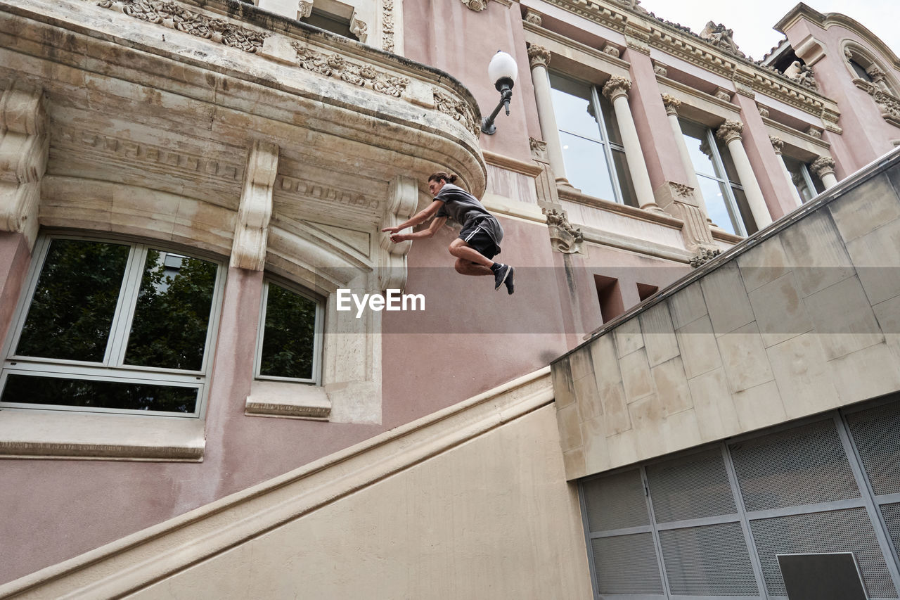 Focused young male jumping over stone steps in city while doing parkour and showing trick