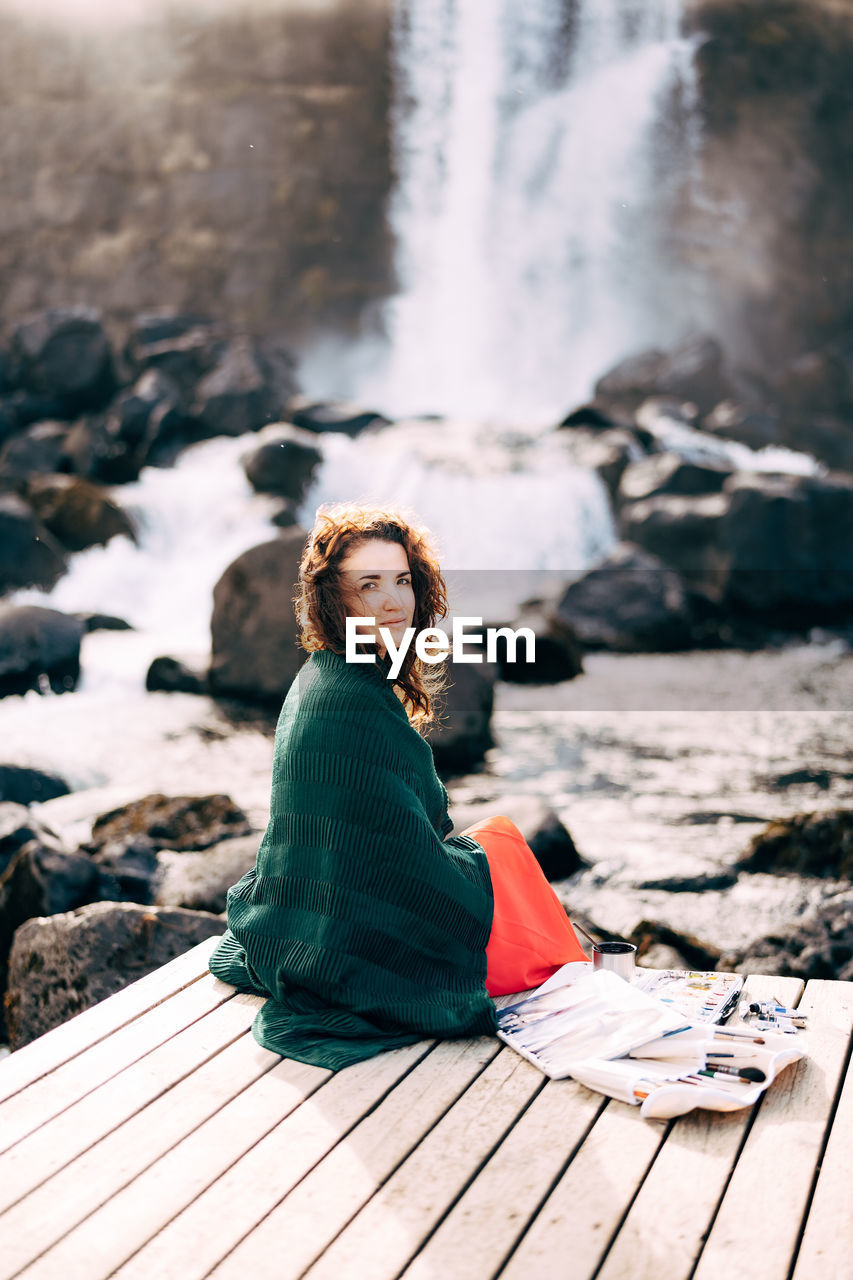 PORTRAIT OF YOUNG WOMAN SITTING ON ROCK