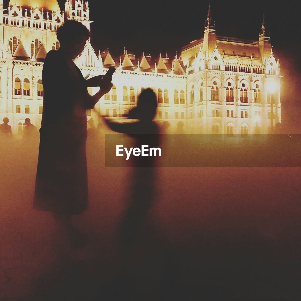 Blurred image of mother and child on field against illuminated building