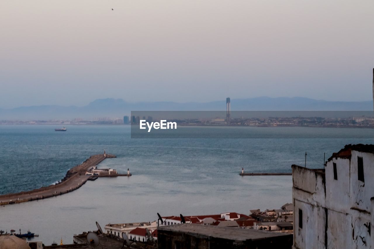 HIGH ANGLE VIEW OF SEA BY BUILDINGS AGAINST SKY
