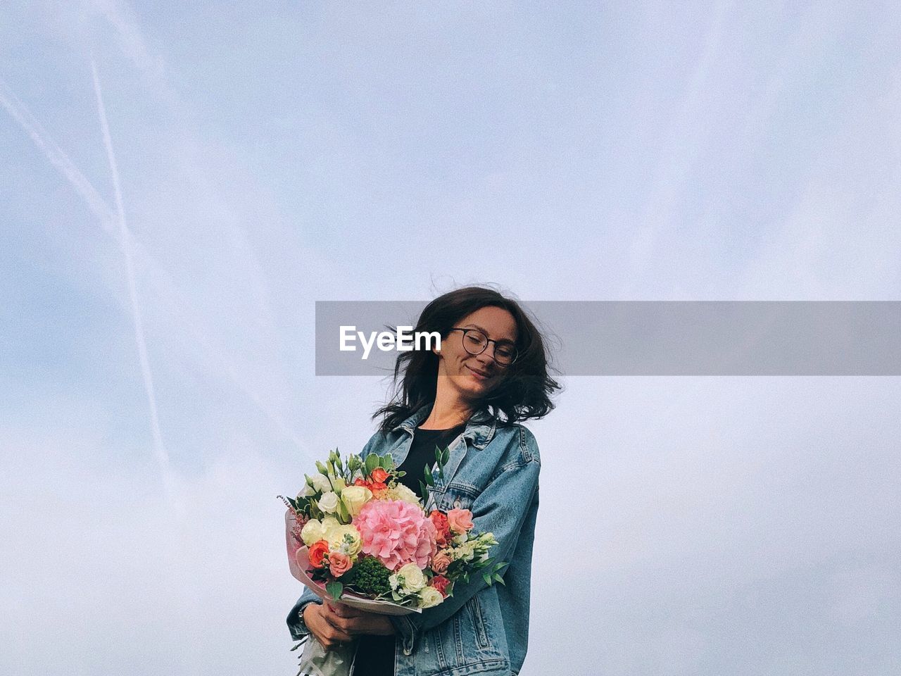 YOUNG WOMAN HOLDING UMBRELLA STANDING BY FLOWER AGAINST SKY