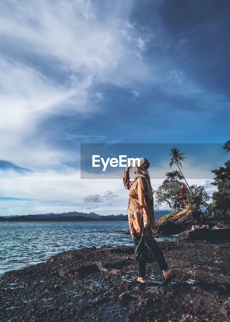 Side view of woman standing by sea against sky