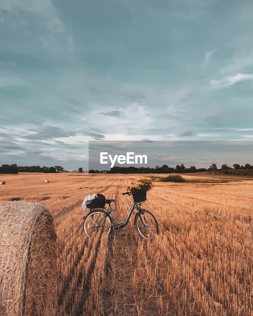 Bicycle and hay bale on field against sky