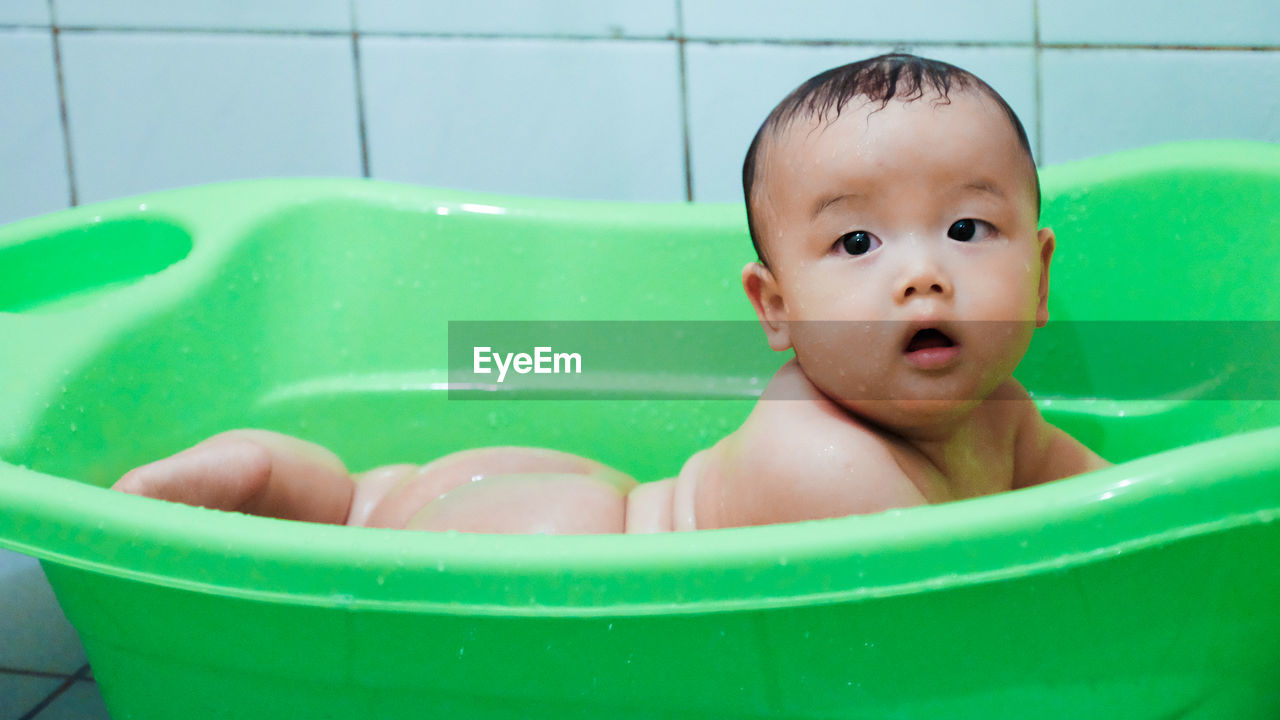 Cute wet baby in green plastic bathtub