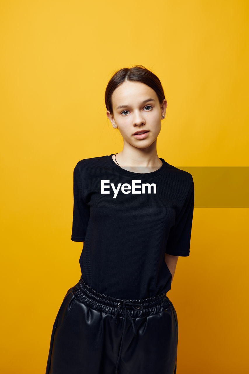 portrait of smiling young woman standing against yellow background