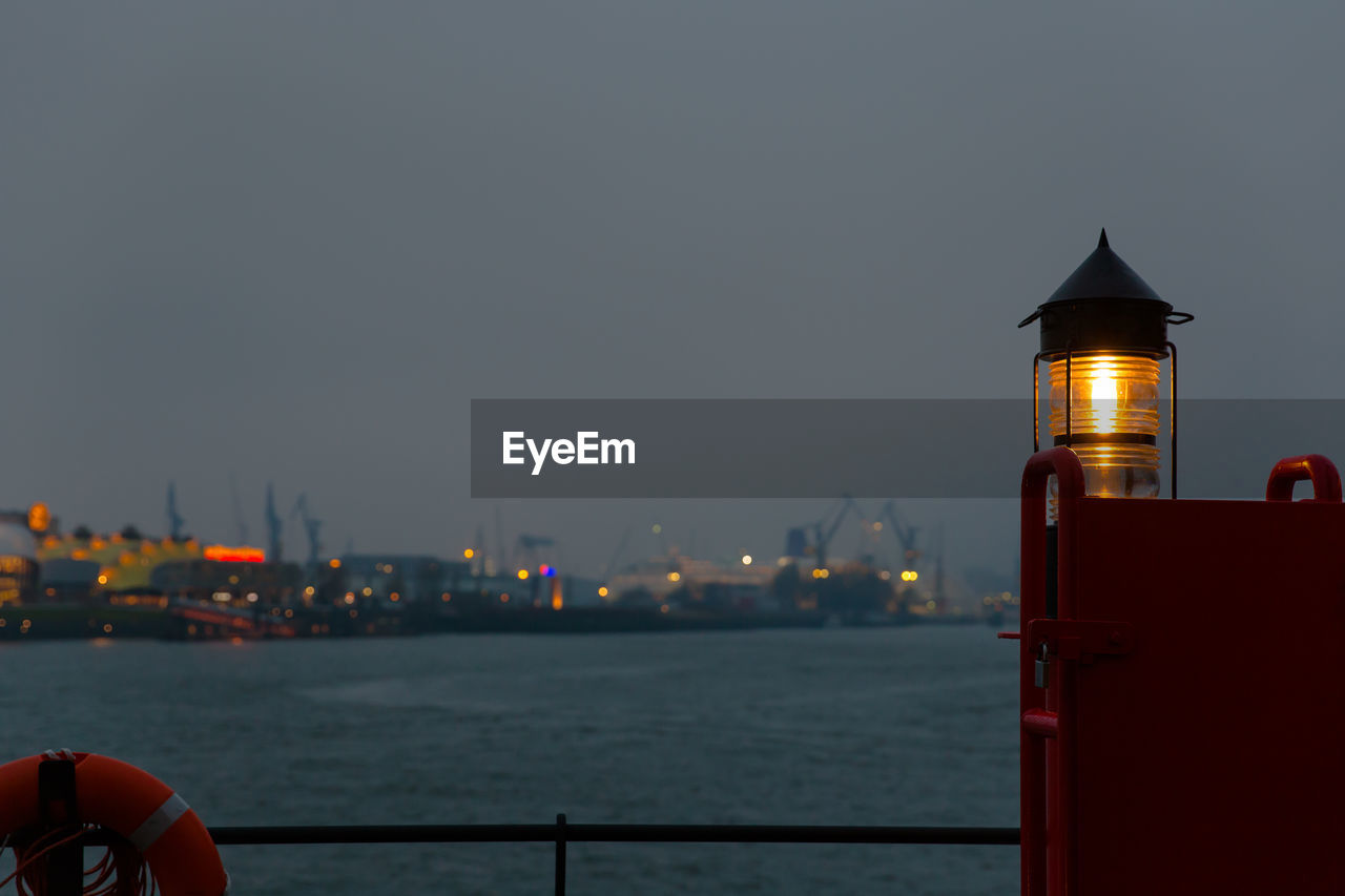 Illuminated lighthouse by elbe river against sky in city at dusk