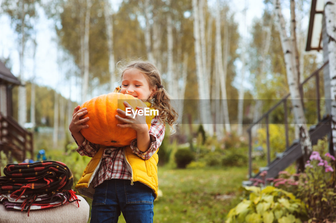 Smiling girl holding pumpkin while standing on field