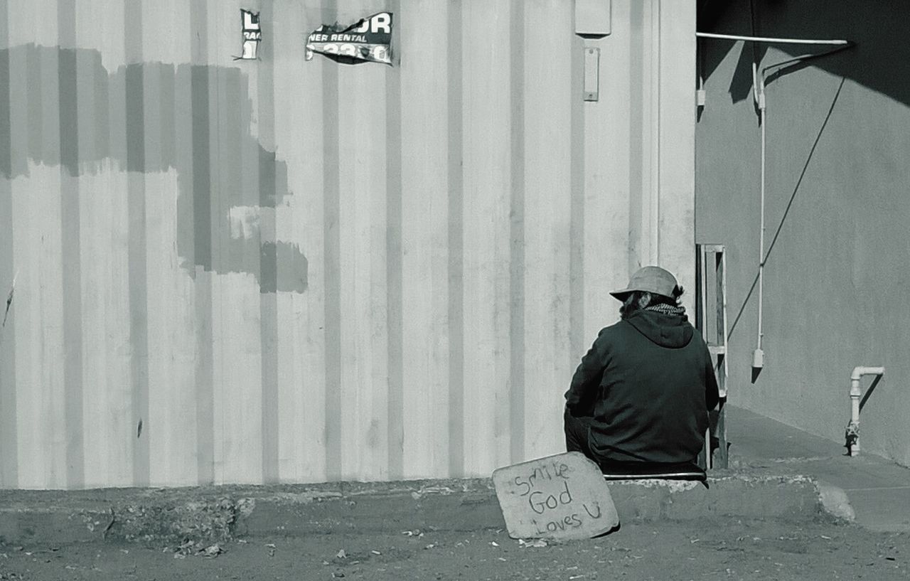 Rear view of homeless man sitting by text against wall