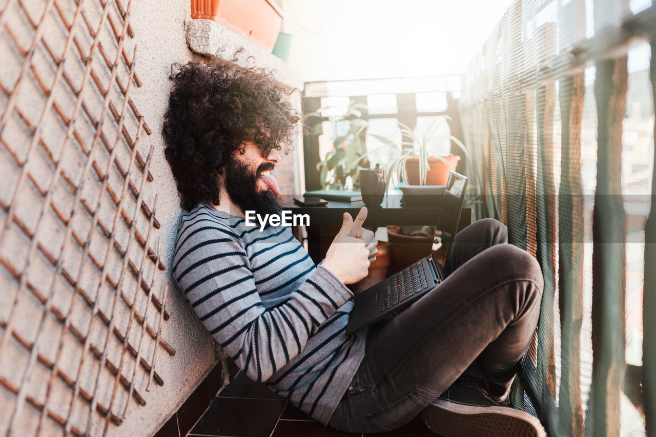 Side view of man gesturing while using laptop in balcony