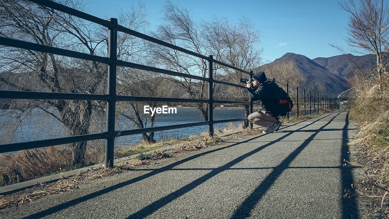 Side view of man photographing while crouching on footpath