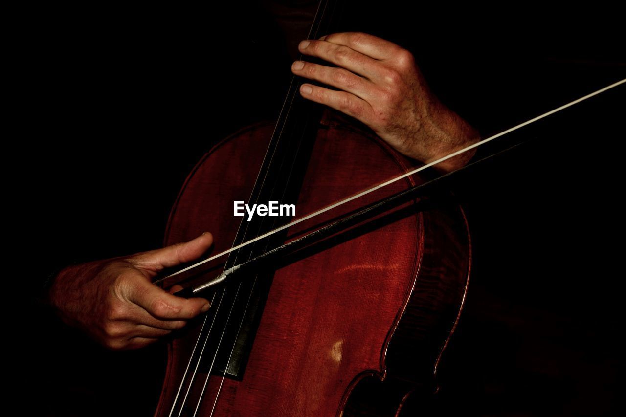 Close-up of man playing cello against black background