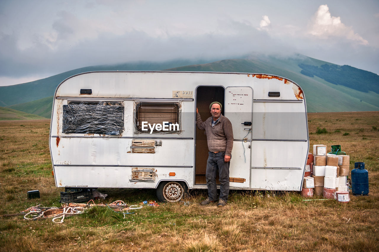 Man standing with travel trailer on mountain against sky