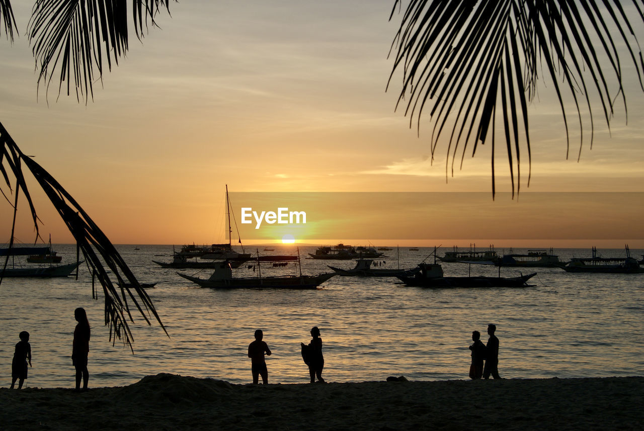 water, sea, sky, sunset, beach, palm tree, silhouette, nature, tropical climate, land, beauty in nature, group of people, ocean, horizon, scenics - nature, evening, horizon over water, shore, nautical vessel, dusk, body of water, men, vacation, coast, trip, tranquility, tranquil scene, holiday, idyllic, sunlight, transportation, sun, lifestyles, tree, travel destinations, outdoors, wave, leisure activity, travel, sand, adult, group, women, tropics, cloud