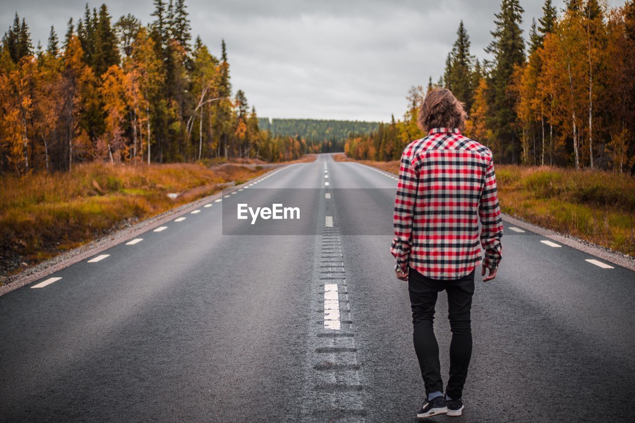 REAR VIEW OF MAN WALKING ON ROAD AMIDST TREES