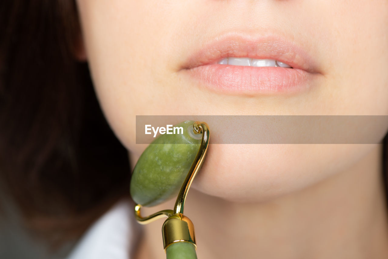 Close up of young woman with jade face roller. she is doing beauty facial massage therapy