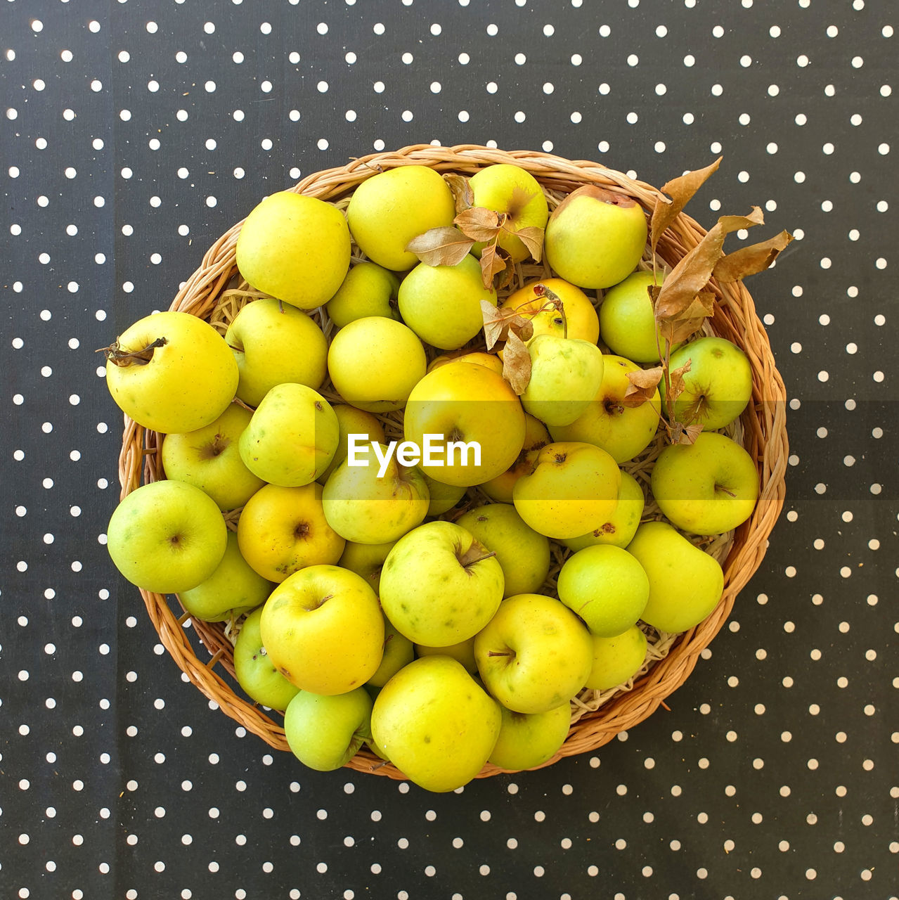 Fresh green apples in round basket on polka dot tablecloth