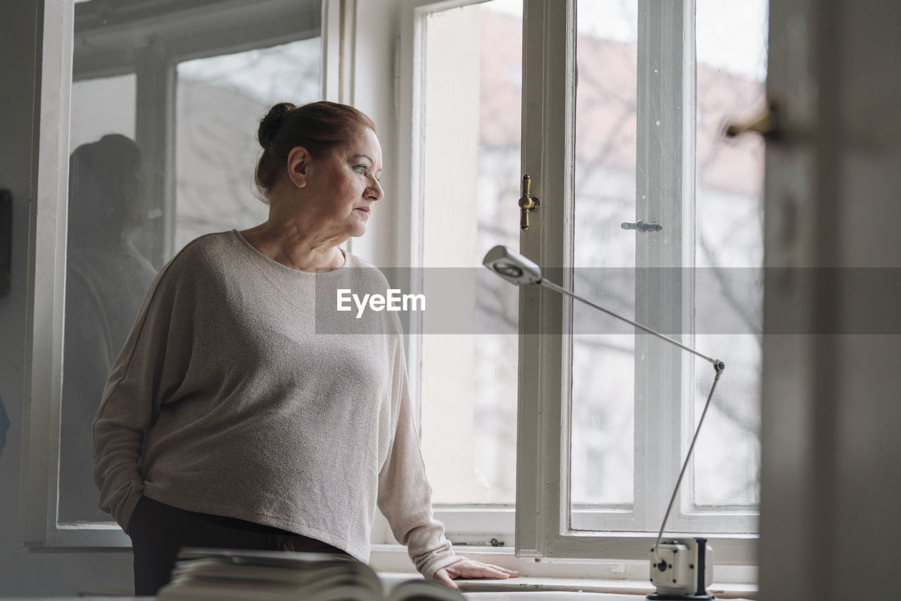 Serious senior woman looking out of window at home