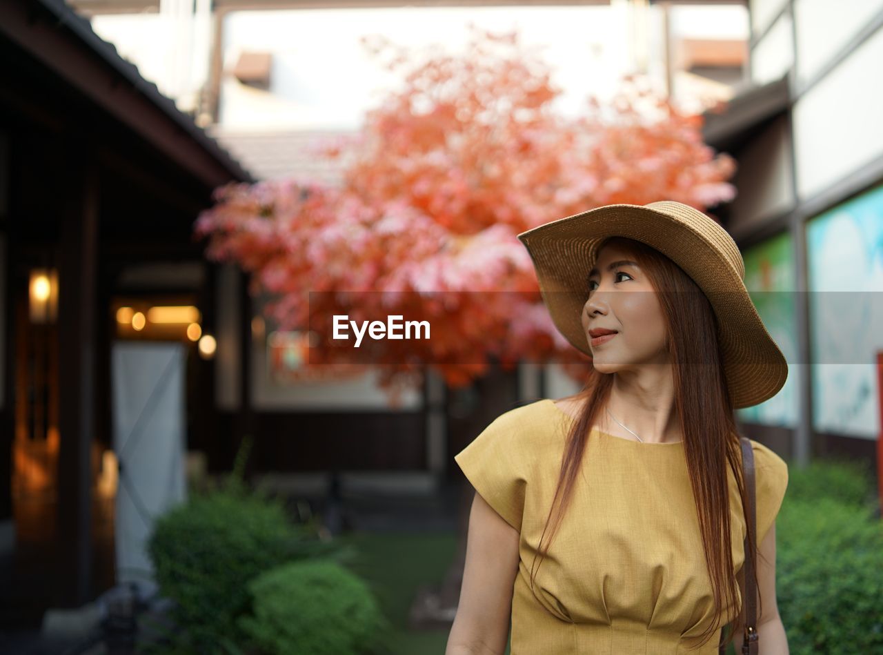 Woman looking away while standing against trees